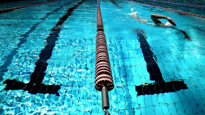 A person swimming in a clear blue outdoor pool with lane dividers.